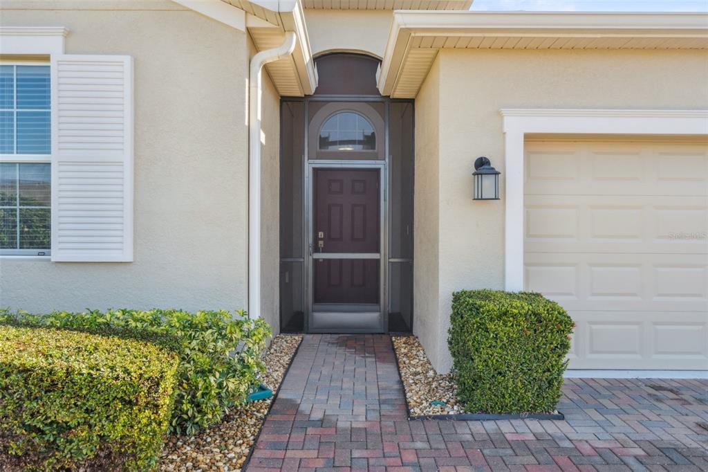 The exterior of a house features a paved walkway leading to a screened front door — 2733 ATTWATER LOOP, WINTER HAVEN, FL
