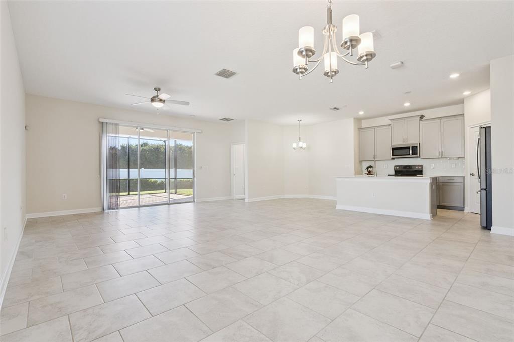 An open-concept living and dining area features light tile flooring, a kitchen, and sliding doors — 2733 ATTWATER LOOP, WINTER HAVEN, FL