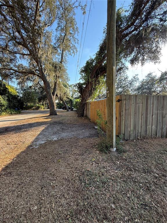 A wooden utility pole stands beside a wooden fence and large trees near a dirt road — LAKESIDE DRIVE, BRANDON, FL