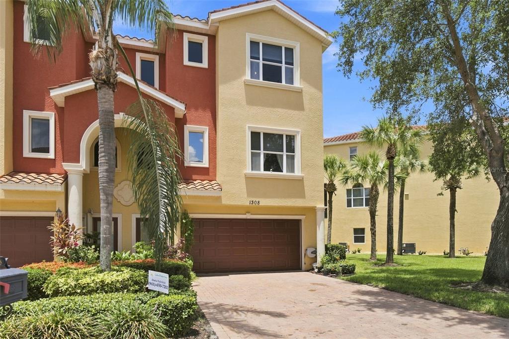 A three-story house with a two-car garage, stucco exterior, and palm trees in the front yard — 1308 3RD STREET CIRCLE E, PALMETTO, FL