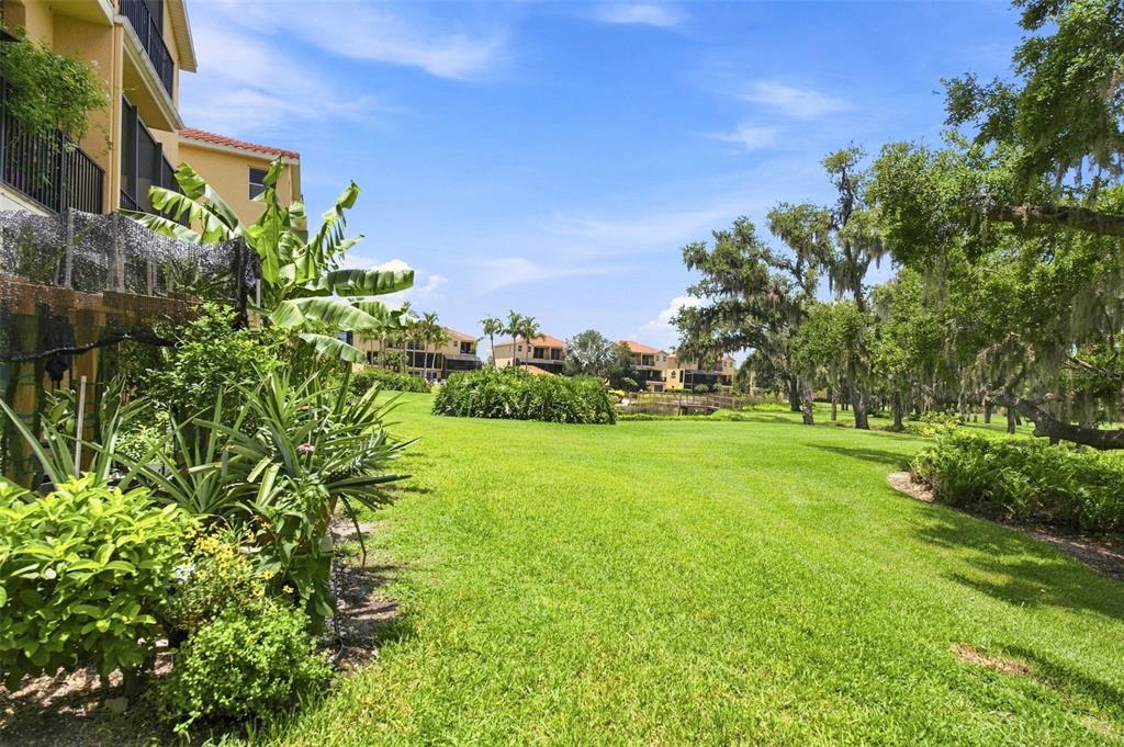 A grassy lawn extends toward a pond and apartment buildings under a bright blue sky — 1308 3RD STREET CIRCLE E, PALMETTO, FL