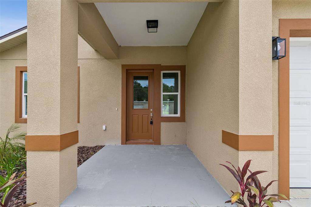 A tan house exterior features a covered entryway with a brown door and window — 2523 AVENUE E SW, WINTER HAVEN, FL