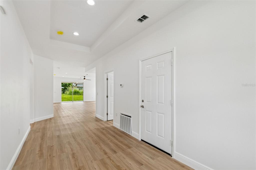 A hallway with light wood-look flooring leads to an open living area with sliding doors — 2523 AVENUE E SW, WINTER HAVEN, FL