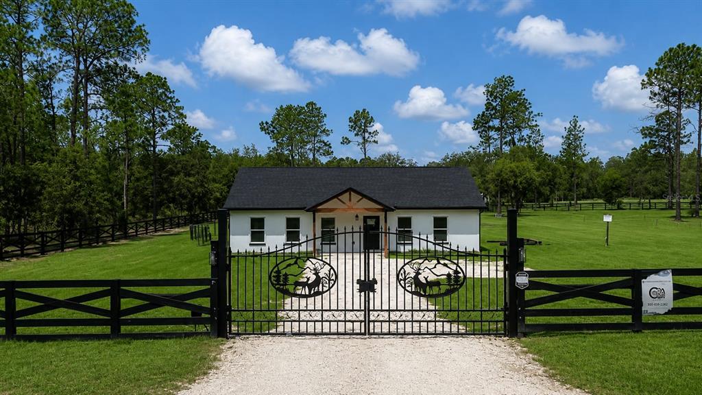 A white house with a black roof sits behind a decorative metal gate and fence — 11670 SE 55TH LANE, MORRISTON, FL