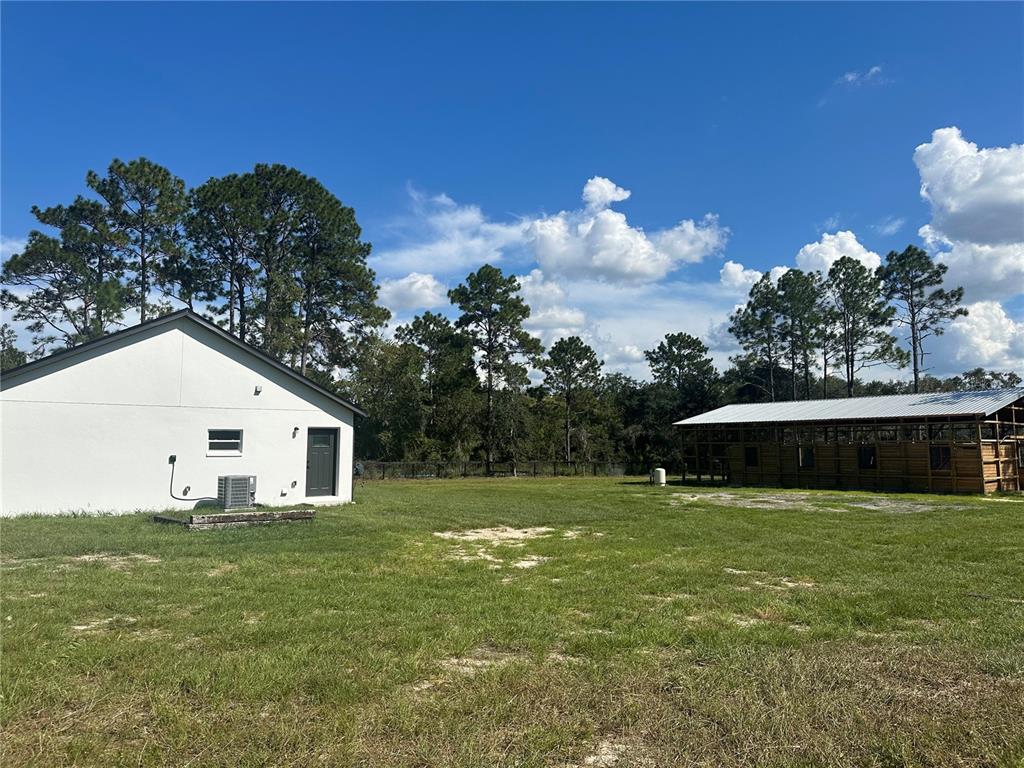A white house and a wooden barn stand on a grassy lot under a blue sky — 11670 SE 55TH LANE, MORRISTON, FL