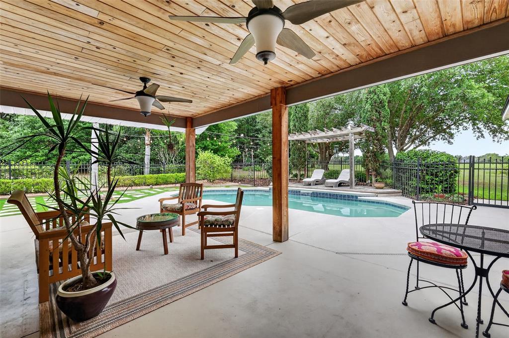 A covered patio features a wood-plank ceiling, ceiling fans, and a view of a swimming pool — 20514 BILL COLLINS ROAD, EUSTIS, FL