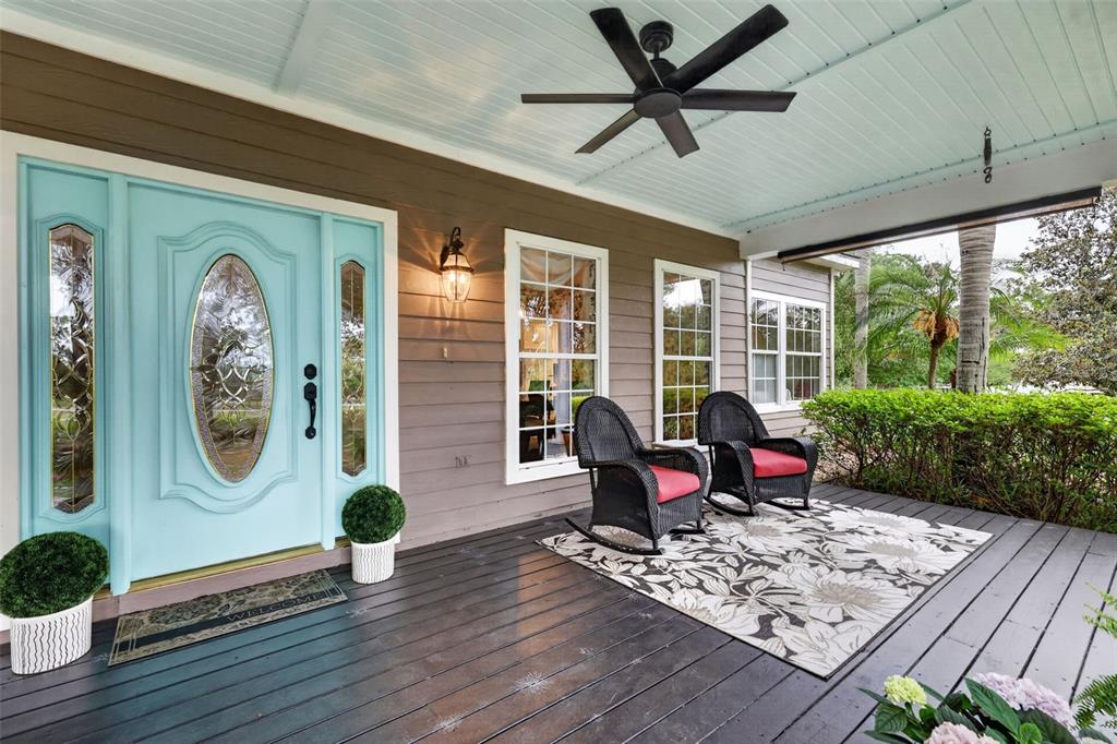 A covered porch features a light blue front door, dark wood decking, and two rocking chairs — 20514 BILL COLLINS ROAD, EUSTIS, FL
