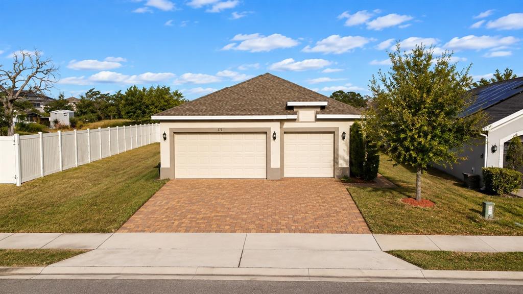 A beige house with a three-car garage and a paver driveway under a blue sky — 179 BLUE CYPRESS DRIVE, DAVENPORT, FL