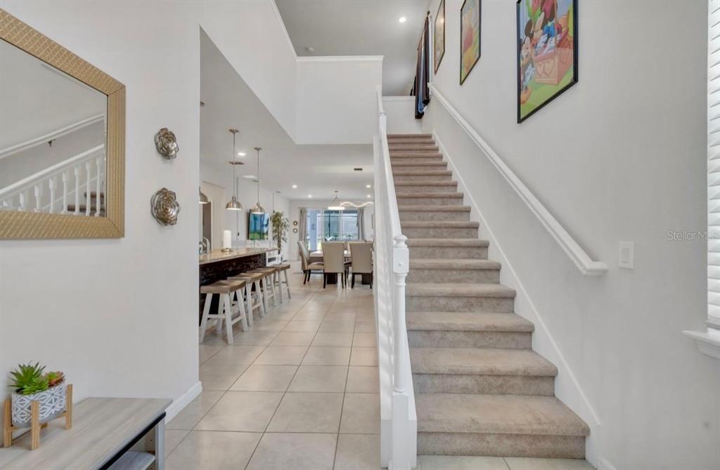 A carpeted staircase leads to an upper level next to an open-concept kitchen and dining area — 7204 OAKMOSS LOOP, DAVENPORT, FL