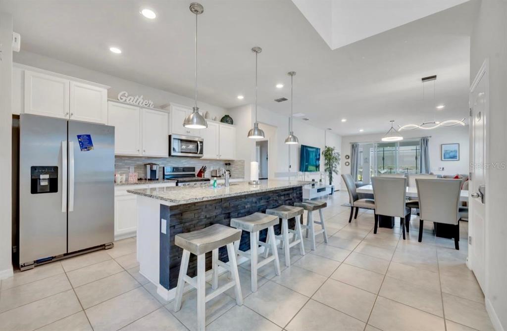 A modern kitchen features a stone-front island, white cabinetry, and an adjacent dining area — 7204 OAKMOSS LOOP, DAVENPORT, FL