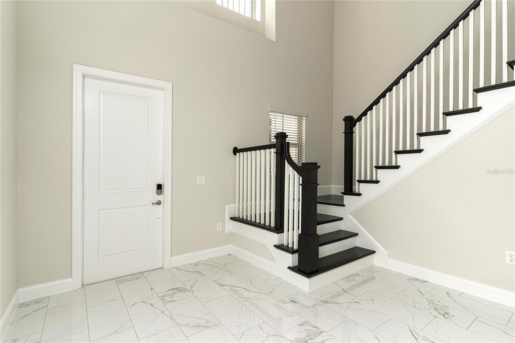 A foyer features white marble-look tile flooring, a white door, and a black-railed staircase — 10152 ROYAL ISLAND COURT, ORLANDO, FL