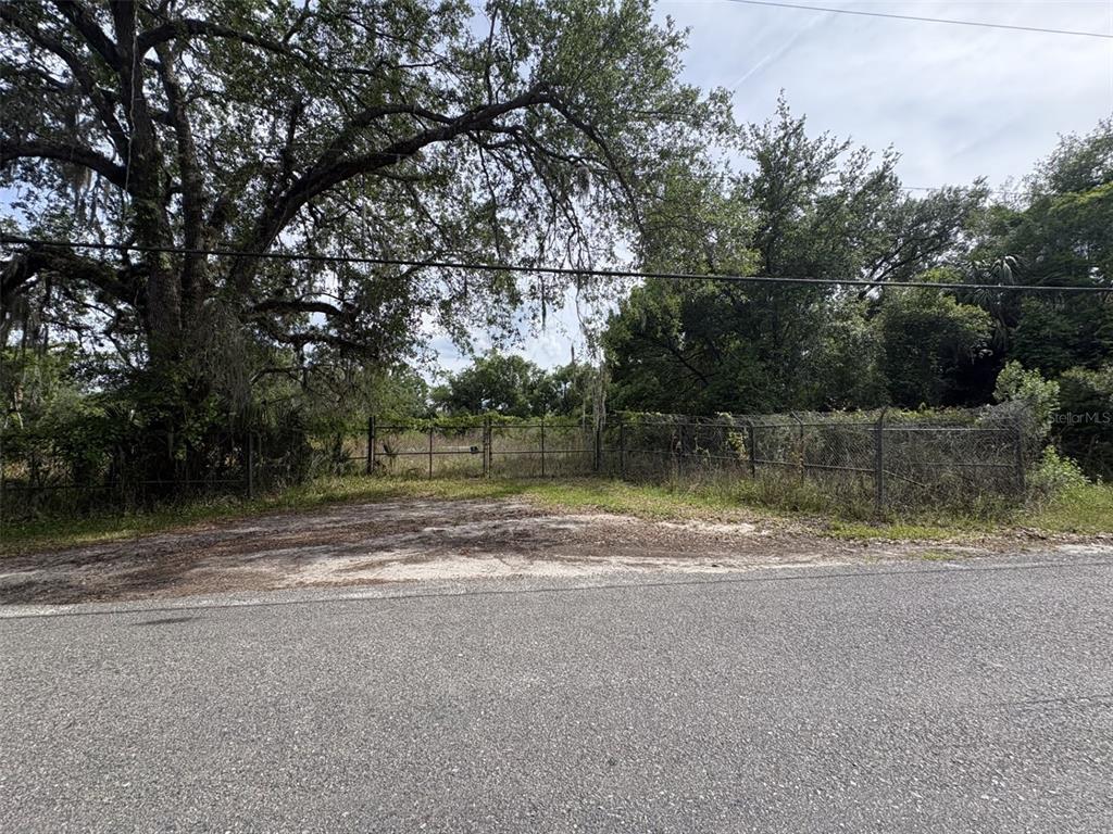 A gravel driveway leads to a chain-link fence bordering a wooded lot — 101 COLLINS ROAD, OSTEEN, FL