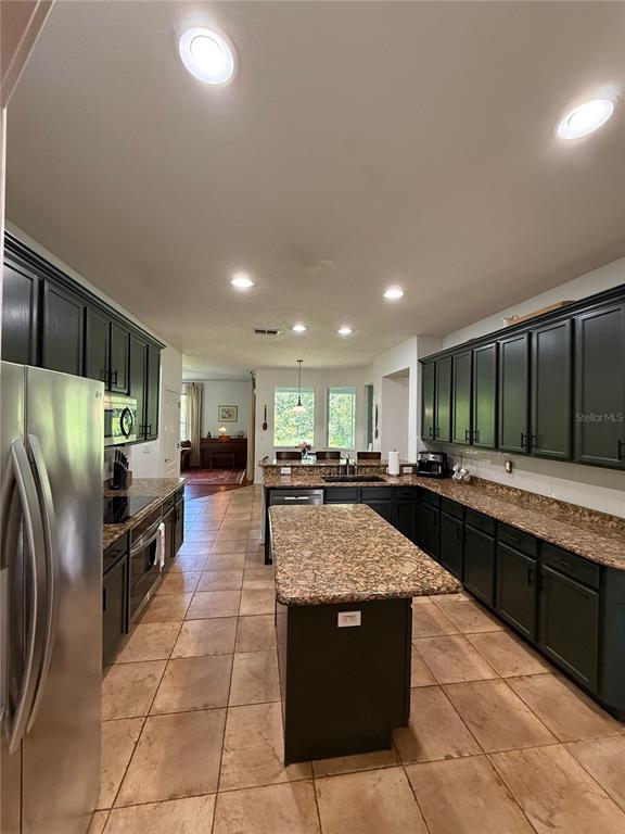 A kitchen features dark cabinets, granite countertops, a central island, and tile flooring — 26620 SHOREGRASS DRIVE, WESLEY CHAPEL, FL