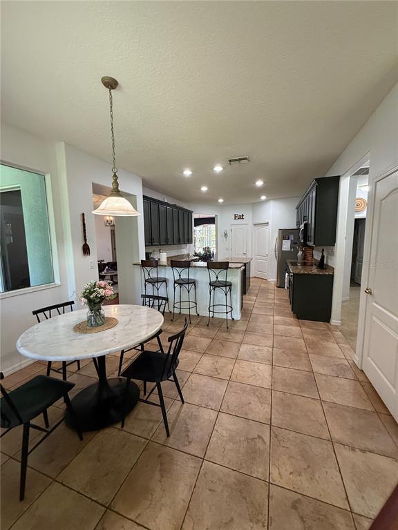 This kitchen features dark cabinetry, a marble-topped dining table, and light-colored tile flooring — 26620 SHOREGRASS DRIVE, WESLEY CHAPEL, FL