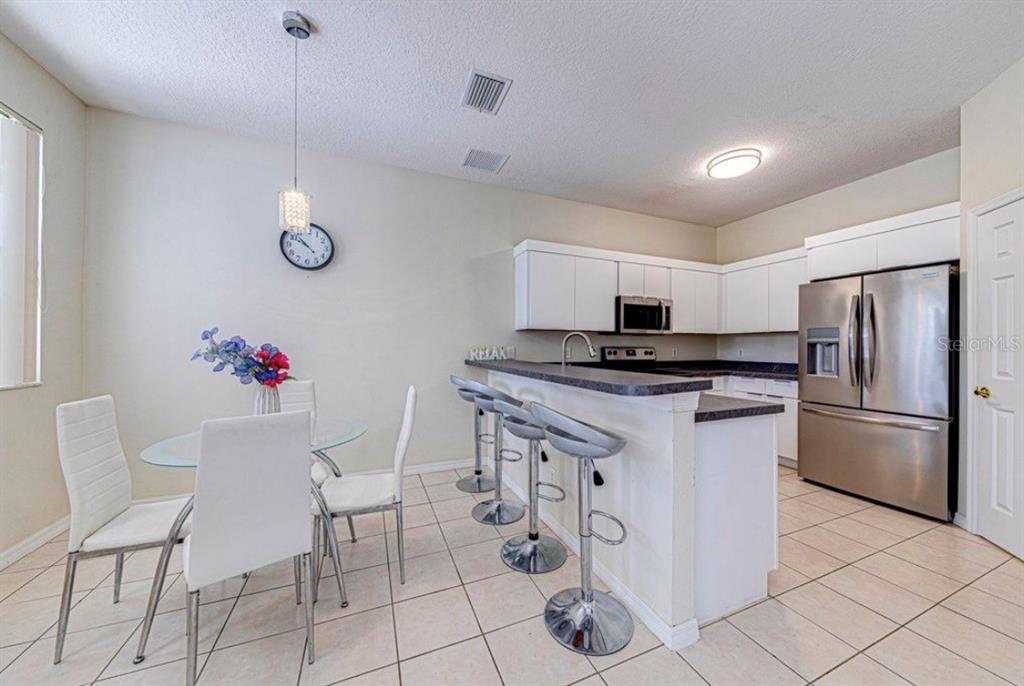 A kitchen with white cabinets, stainless steel appliances, a breakfast bar, and a dining area — 360 TUPELO CIRCLE, DAVENPORT, FL