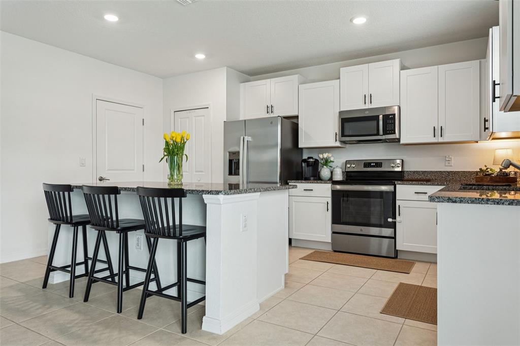 A kitchen features white cabinets, stainless steel appliances, a granite island, and three black stools — 11693 LAVENDER LOOP, SPRING HILL, FL
