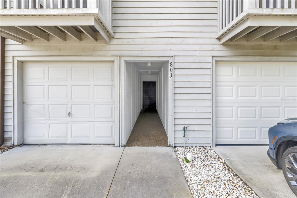 A narrow hallway with white walls and wood-look flooring leads to a set of stairs — 6462 92ND PLACE N UNIT 803, PINELLAS PARK, FL