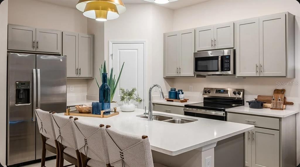 A kitchen with gray cabinets, stainless steel appliances, and a white quartz island with seating — 2513 BALMERINO WAY UNIT 0, MOUNT DORA, FL