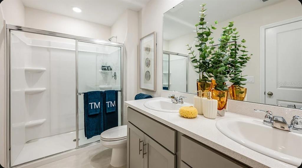 A bathroom features a double vanity with gray cabinets, a glass-enclosed shower, and a toilet — 2513 BALMERINO WAY UNIT 0, MOUNT DORA, FL
