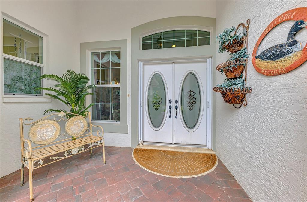 A covered entryway features a brick patio, a metal bench, double doors, and wall decor — 625 MISTY PINE DRIVE, VENICE, FL