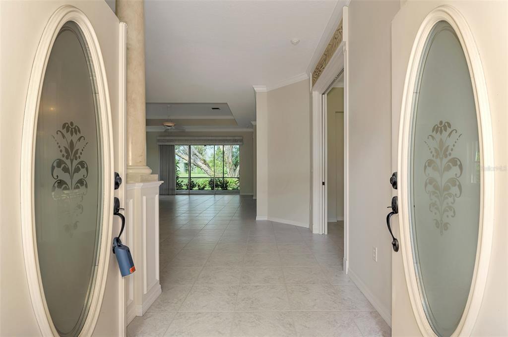 A view from an entryway looking through a tiled hallway toward a living room — 625 MISTY PINE DRIVE, VENICE, FL