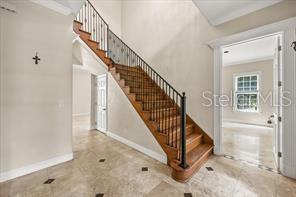 An interior foyer features a wooden staircase with a black metal railing and tile flooring — 3620 LEOTA DRIVE, APOPKA, FL