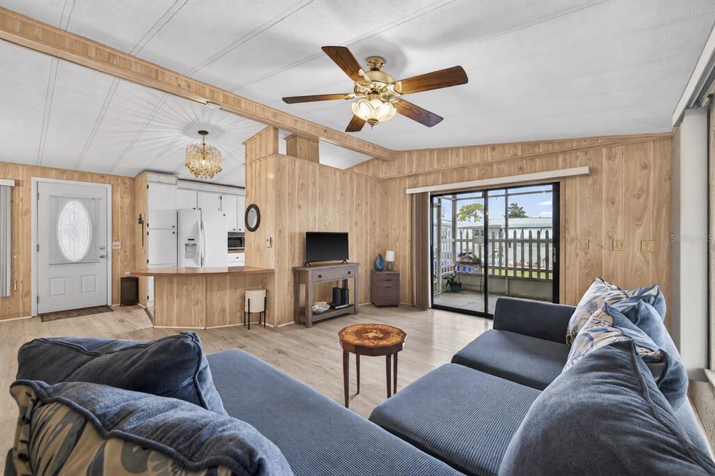 A living room features wood-paneled walls, a ceiling fan, and a view of a patio — 7880 54TH AVENUE N UNIT 38, ST PETERSBURG, FL