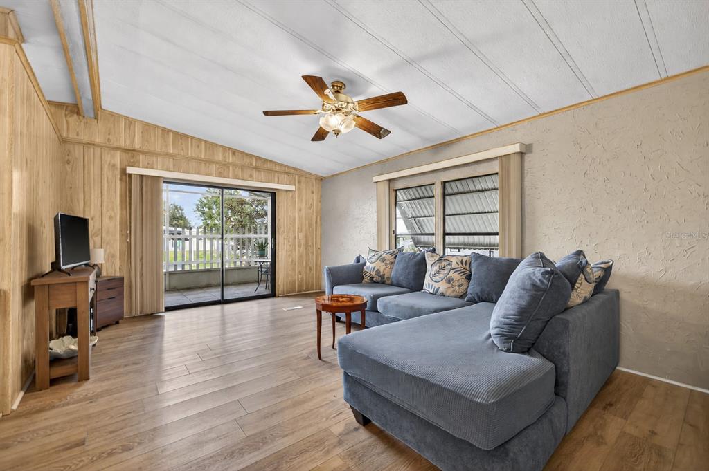 A living room features wood-look flooring, a blue sectional sofa, and a sliding glass door — 7880 54TH AVENUE N UNIT 38, ST PETERSBURG, FL