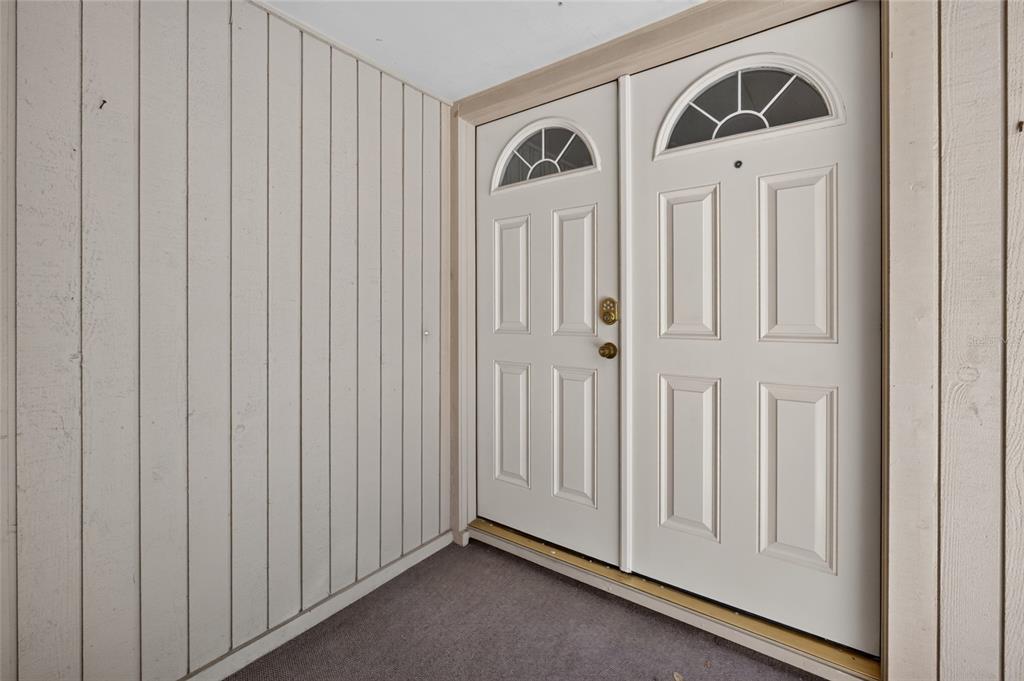 A beige double door entrance with arched windows sits on a covered porch with siding — 100 HIDDEN OAK DRIVE, LONGWOOD, FL
