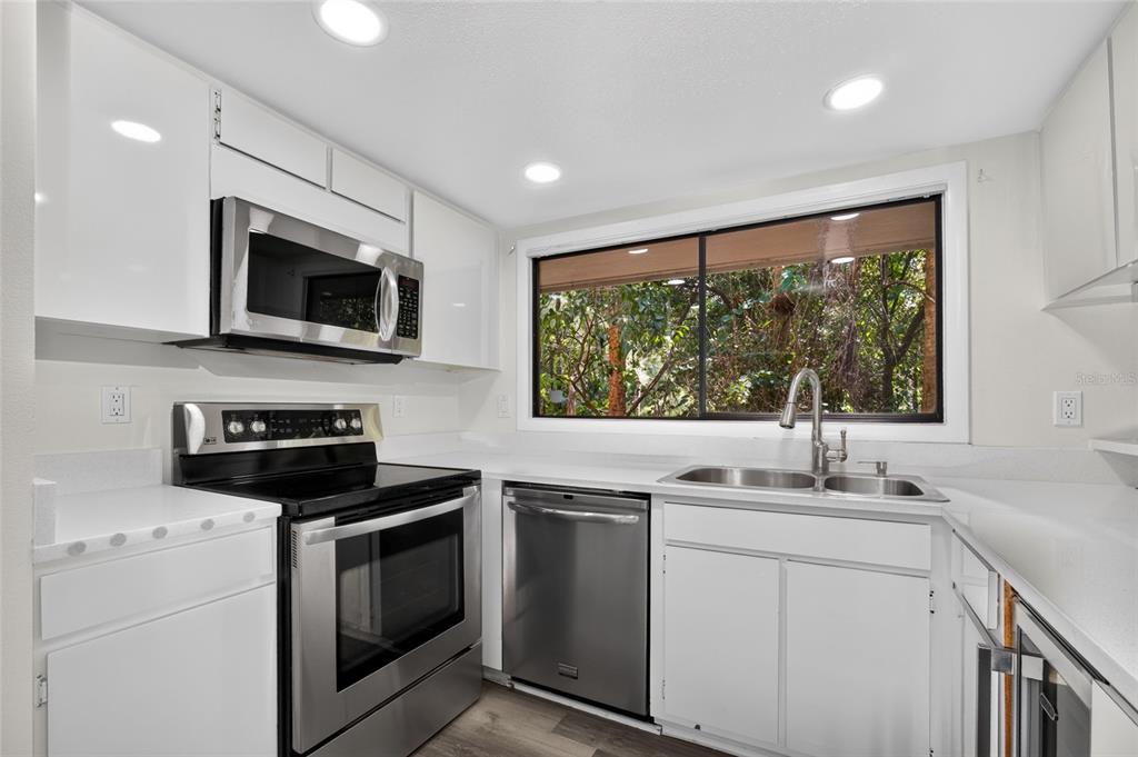 A kitchen with white cabinets, stainless steel appliances, and a window overlooking trees — 100 HIDDEN OAK DRIVE, LONGWOOD, FL