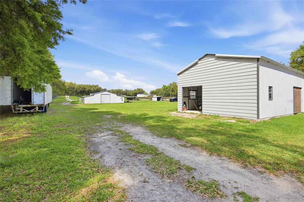 A grassy field features a metal workshop, a smaller shed, and a trailer under trees — 3660 W HWY 329, REDDICK, FL