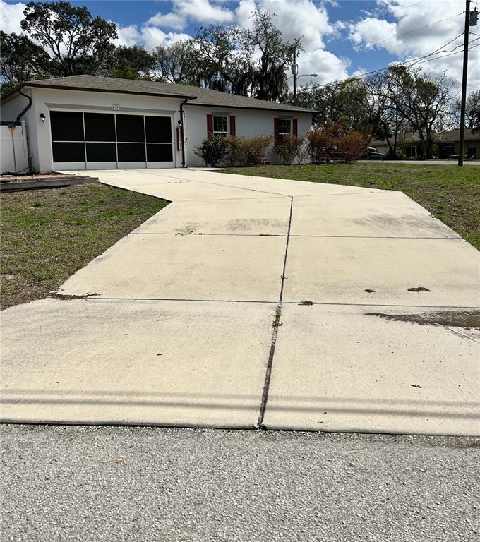 A single-story house with a white exterior, a garage, and a large concrete driveway — 4096 THUNDERBIRD AVENUE, SPRING HILL, FL