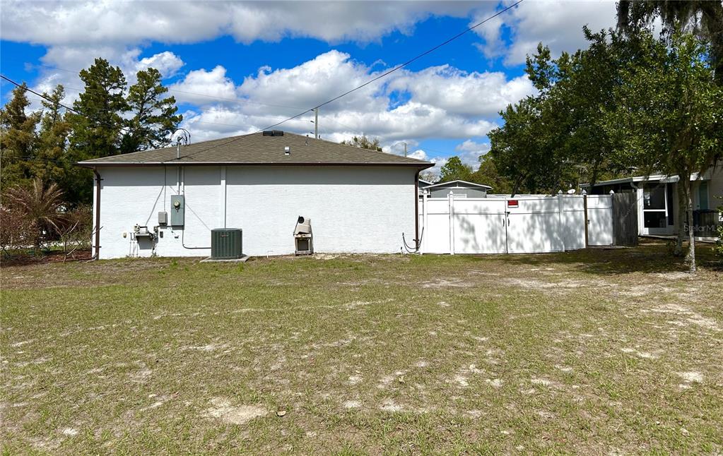 The exterior of a single-story house features a white stucco wall, a dark roof, and a fence — 4096 THUNDERBIRD AVENUE, SPRING HILL, FL