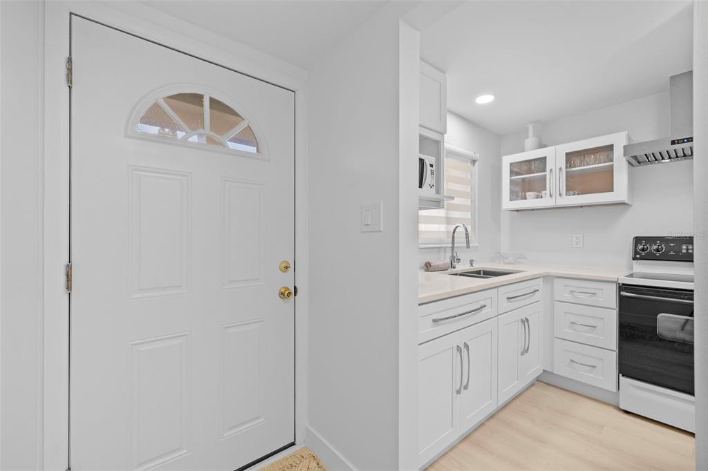 A white front door opens into a kitchen featuring white cabinets, light countertops, and appliances — 4126 HERON WAY UNIT B113, BRADENTON, FL