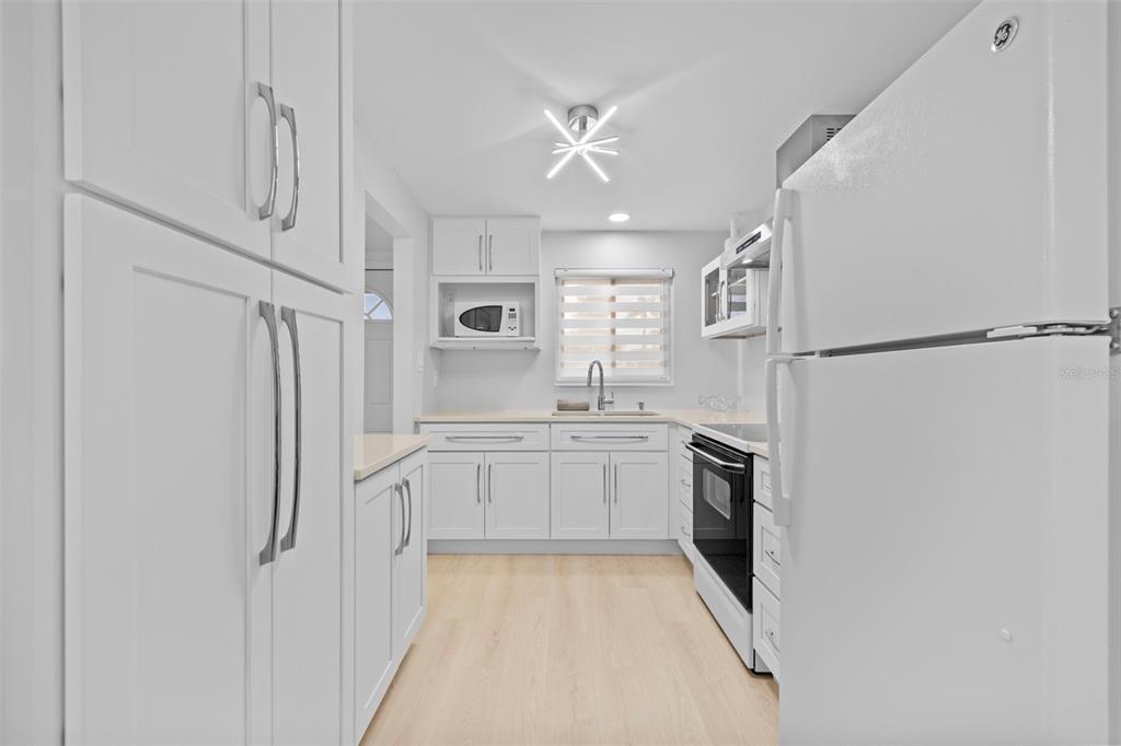 A bright kitchen features white cabinets, light wood flooring, and white appliances — 4126 HERON WAY UNIT B113, BRADENTON, FL