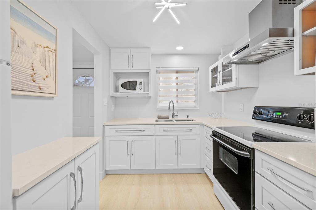A bright kitchen features white cabinetry, light countertops, a stainless steel range, and a microwave — 4126 HERON WAY UNIT B113, BRADENTON, FL