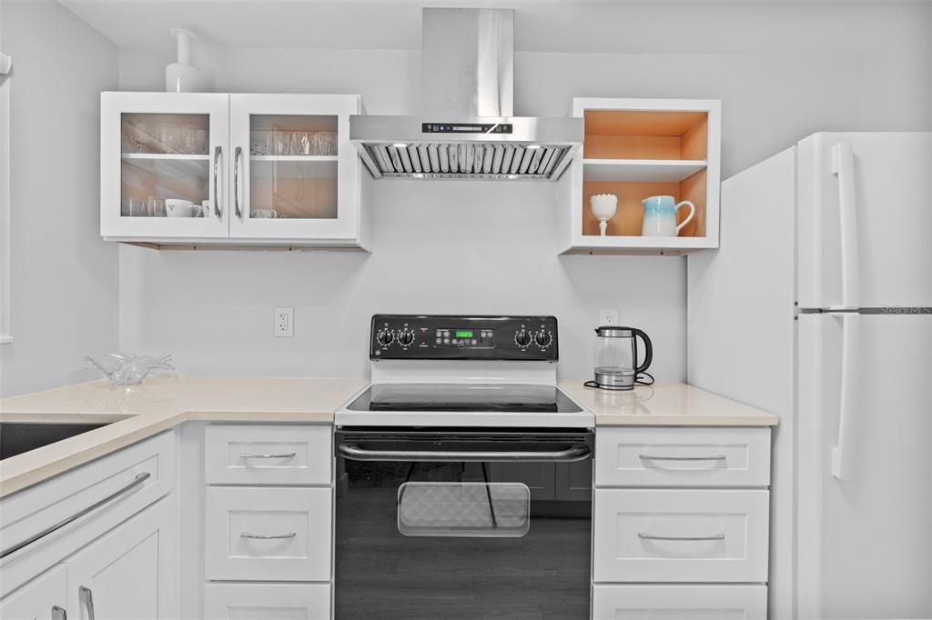 A kitchen features white cabinets, a stainless steel range hood, and a white electric stove — 4126 HERON WAY UNIT B113, BRADENTON, FL