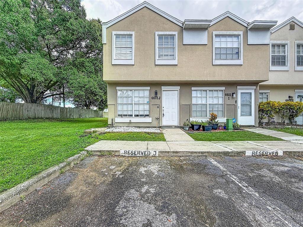 A two-story townhouse exterior features tan stucco walls, white trim, and reserved parking spaces — 6601 121ST AVENUE UNIT J, LARGO, FL