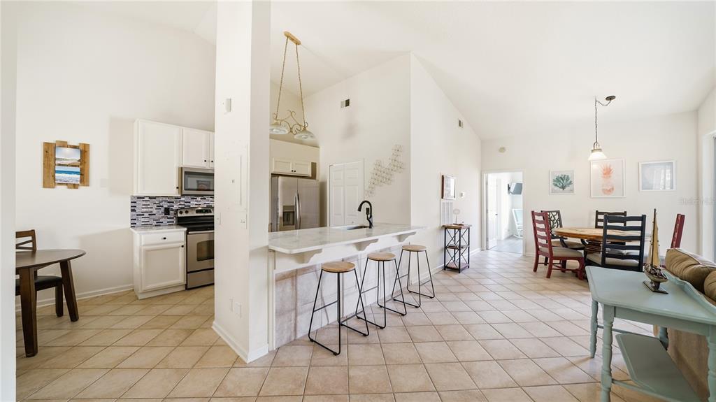 A kitchen with white cabinets and a breakfast bar overlooks a dining and living area — 705 AUGUSTA CIRCLE UNIT 705, ST AUGUSTINE, FL