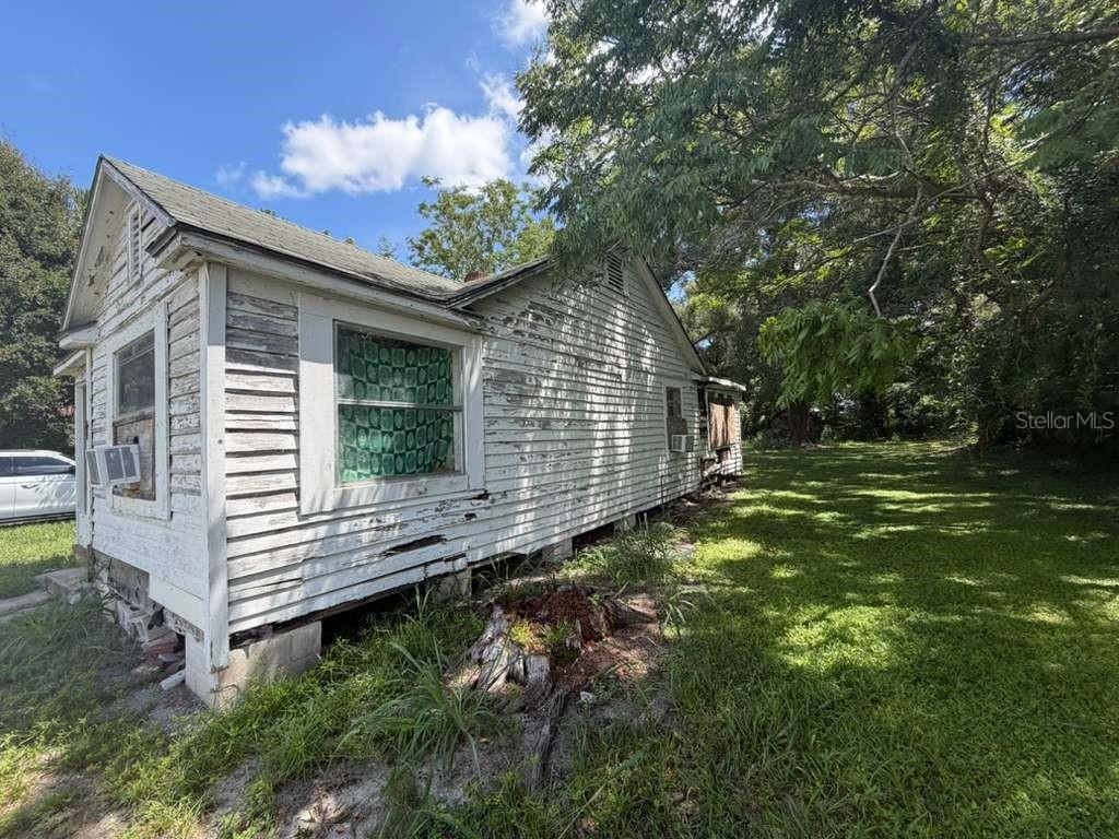 A weathered, white wood-sided house sits on a grassy lot with a large tree nearby — 410 N ORANGE AVE, UMATILLA, FL