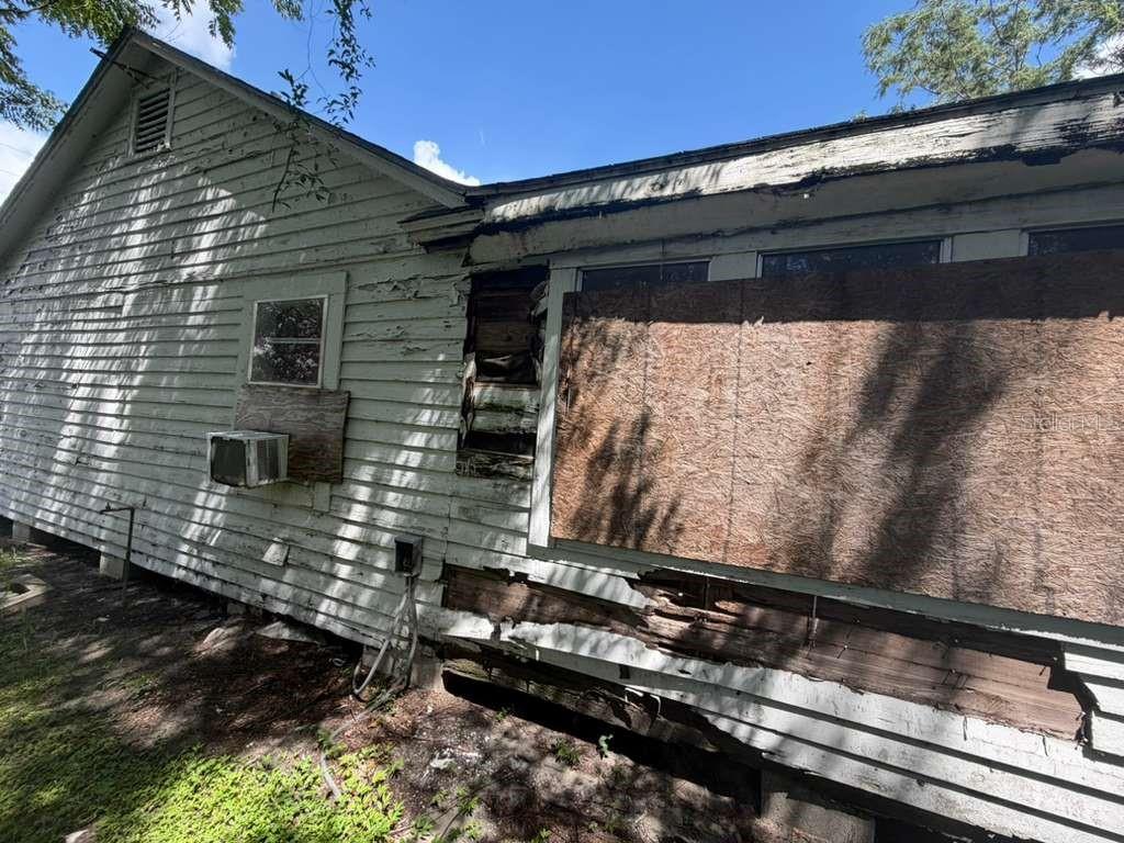 The exterior of a weathered house features peeling white siding, boarded-up windows, and significant wood rot — 410 N ORANGE AVE, UMATILLA, FL