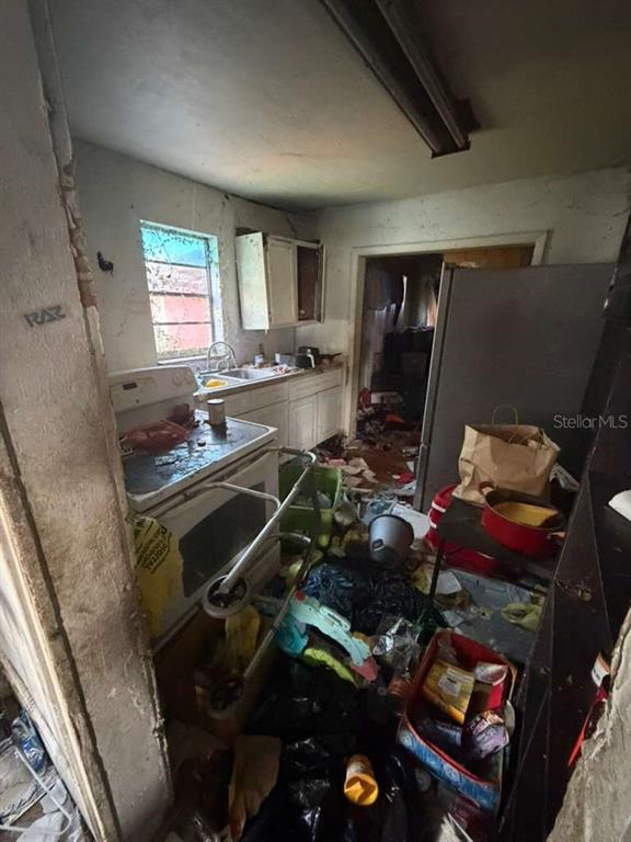 A cluttered, dilapidated kitchen with a stove, sink, and debris-covered floor in need of renovation — 410 N ORANGE AVE, UMATILLA, FL