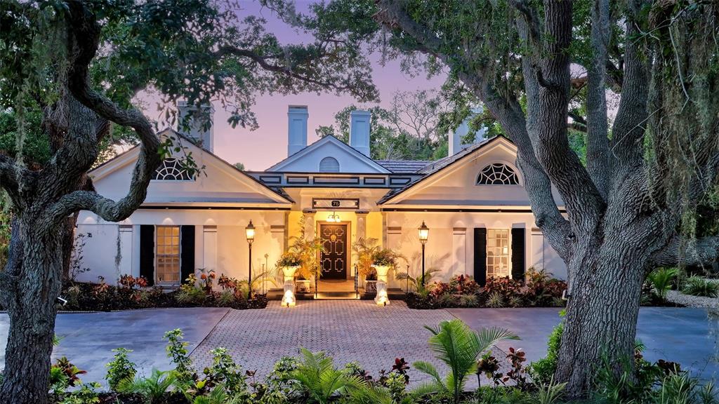 A symmetrical white house with a paved driveway and large oak trees in the foreground — 75 OSPREY POINT DRIVE, OSPREY, FL