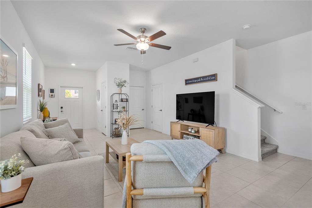 A living room features a light-colored sofa, a television on a wooden stand, and stairs — 6033 ACARA LANE, LAND O LAKES, FL