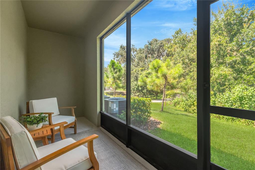 A screened-in porch features two wooden chairs and a view of a grassy yard — 6033 ACARA LANE, LAND O LAKES, FL
