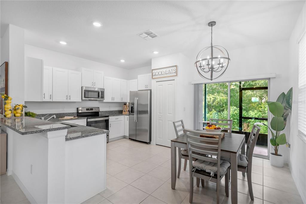 A kitchen and dining area features white cabinets, granite countertops, stainless steel appliances, and tile flooring — 6033 ACARA LANE, LAND O LAKES, FL