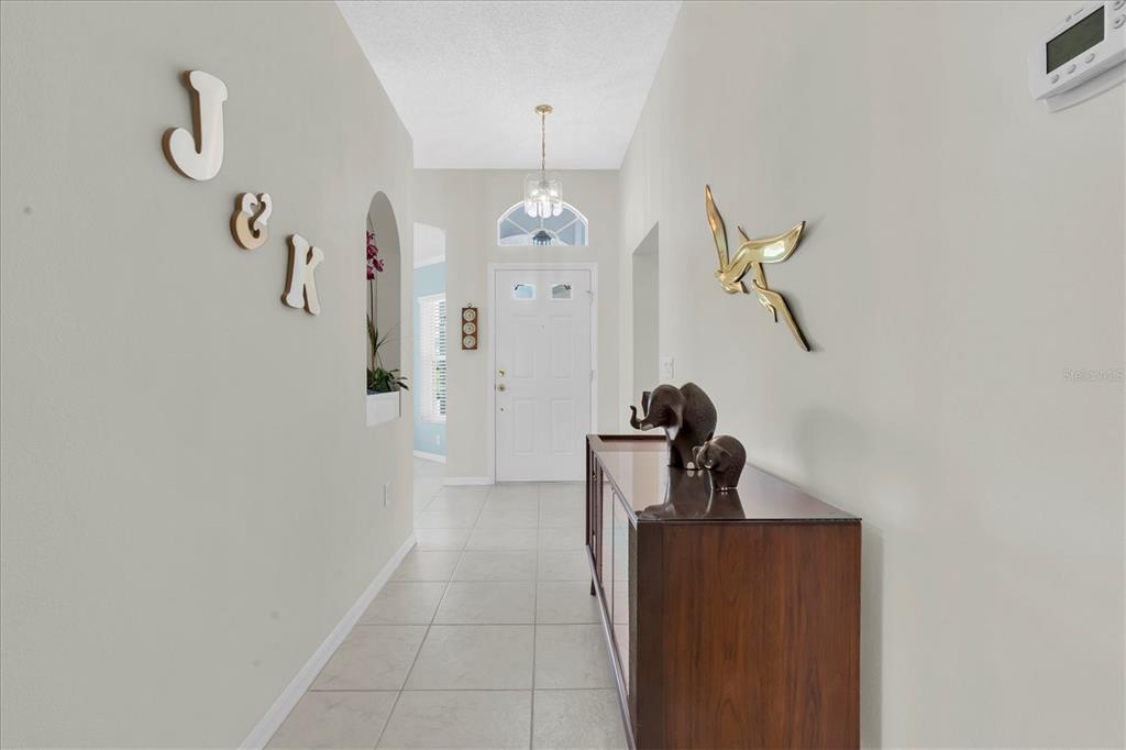 A tiled entryway features a wooden console table, wall decor, and a white front door — 11250 HOLLANDER AVENUE, HUDSON, FL