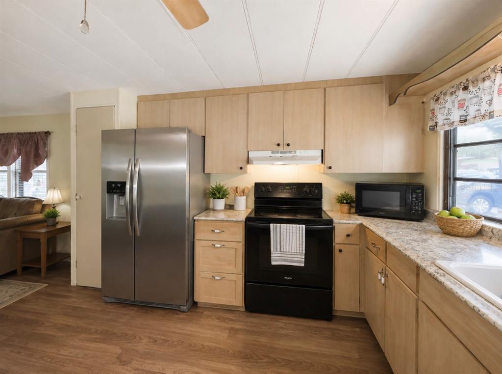 A kitchen with light wood cabinets, stainless steel refrigerator, black stove, and granite-look countertops — 15423 SANTA FE TRL, EUSTIS, FL