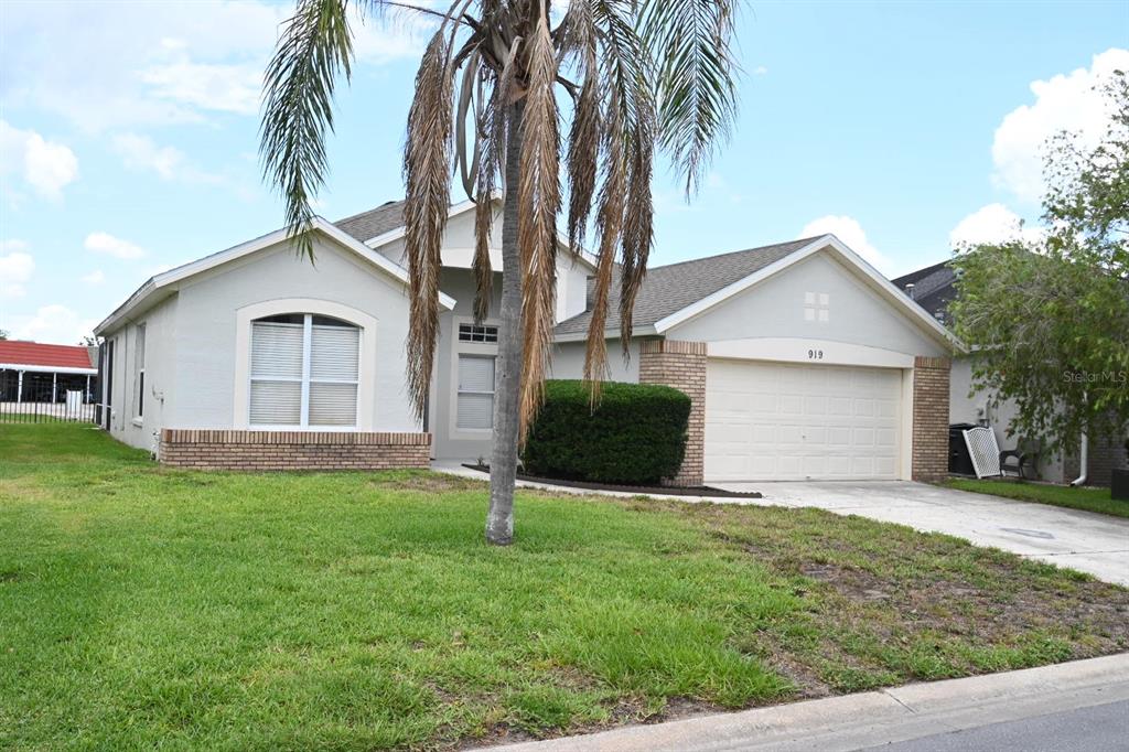 A single-story house with a light-colored stucco exterior, a two-car garage, and a palm tree — 919 JAYBEE AVENUE, DAVENPORT, FL