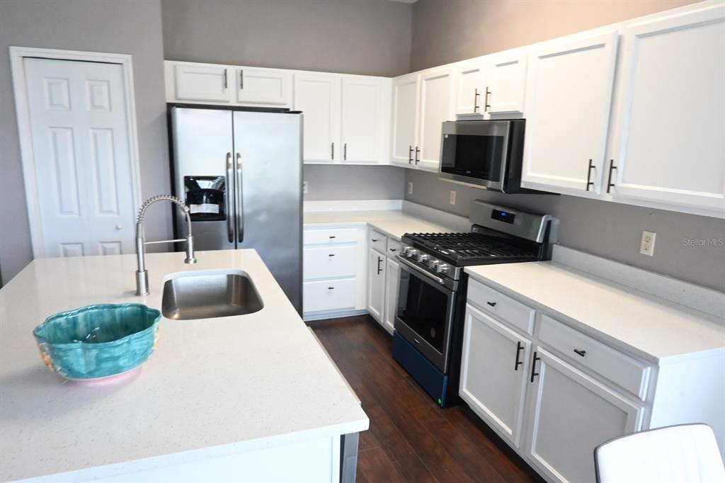A kitchen features white cabinets, stainless steel appliances, a center island, and dark wood flooring — 919 JAYBEE AVENUE, DAVENPORT, FL